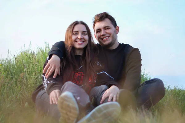 幸せな若いカップルの愛 人々はカメラを見て カップルは草の上に座っています 抱擁とロマンス 本当の感情 幸福と喜び 自然の中でロマンチックなデート — ストック写真