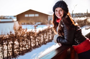 Kış parkında bir kız. Kışlık ceketli, sıcak elbiseli genç bir kadın. Kışın kırmızı ekoseli bir balkonda duruyor ve güneşe bakıyor. Yüz profilindeki balkondaki kız ileriye bakıyor.