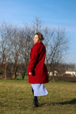 Parktaki sonbahar otlağında yürüyen bir kadın. Kırmızı ceketli bir kız doğasında duruyor. Bir kadın hareketli poz veriyor. Eski moda fotoğraf. Güzel görüntü. Bir kadın üzerini çıkarıyor..