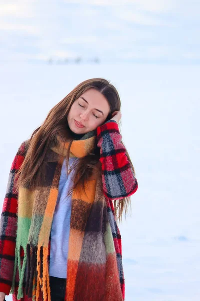 beautiful young woman in winter outdoors.Girl in a warm scarf.Winter portrait.Woman in a red coat.Girl dreams.Woman thinks.Lots of snow.Beautiful girl outdoors in winter.Checkered coat.Stylish clothes.Ukrainian.Emotions of calm.Closed eyes.woman.
