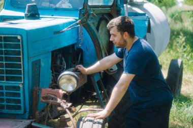 Ot tarlasında çiftçi, traktörlü bir adam, traktörün yanında genç bir çiftçi, doğada duruyor. Acemi çiftçi, çiftçi. Ukrayna 'da çiftçilik. Eski çalışan traktör, tamirci. Traktörün yanındaki adam..