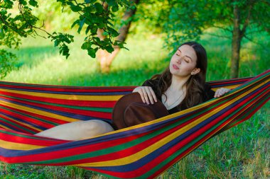 Ormanda hamakta dinlenen genç bir kadın. Esrarengiz. Dinlenen ve rüya gören genç bir kadın. İş ve boş zaman arasındaki denge. Şapkalı bir kız. İyi ruh hali.