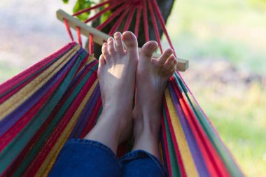 legs on a hammock. outdoor recreation in a hammock. summer vacation. life without gadgets. relaxation from the outside world. good weather and mood. funny toes. striped hammock.summer landscape. legs clipart