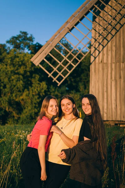 three girlfriends are relaxing in nature against the backdrop of a windmill.best friends.girls on a walk.Friends rest in nature.Three girlfriends smile.Beautiful girls.Strong friendship.hugging.rest