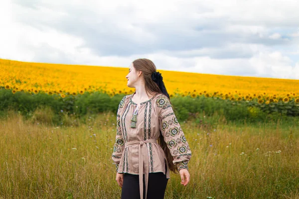 Ukrainian woman in an embroidered shirti n a field of sunflowers.dreaming woman.pensive happy woman.self-confident girl.patriotism.woman on a flowering meadow.a tender girl.Loneliness.pleasure.hair.