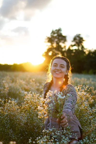 Ukrainian woman in an embroidered shirt sits in a field of daisies at sunset.dreaming woman.pensive happy woman.self-confident girl.patriotism.woman on a flowering meadow.a tender girl.Loneliness.
