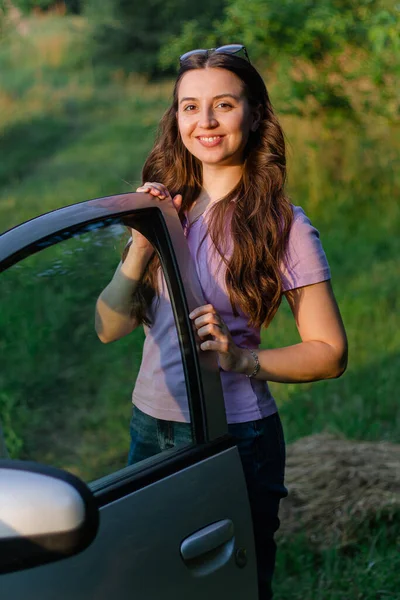 happy smiling female driver with a long hair.happy woman stands near the car.woman driver.car rental.driving school.car instructor woman.travel.Traveling by car.Driver.Auto in nature.Girl sitting in the auto.happy emotions.The girl smiles.