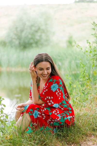 woman thinks.a mysterious lady in red.girl straightens her hair.happy girl.mental health.calmness and balance.not a standard appearance.woman looks away.health care.woman sitting on the shore of pond.