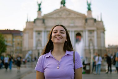 Bir şehirde güzel bir genç kızın portresi. Kadın gülüyor ve poz veriyor Lviv 'deki güzel opera evinin arka planında. Eski bir kasabada turist. Avrupa' da turizm. Kız tatilde. Mutlu turist.