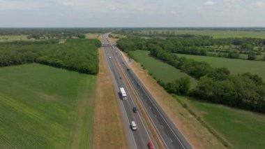 Hollanda, Avrupa 'daki küçük ormanlardan ve açık alanlardan geçen arazi manzarası ve otoyolda giden arabalar üzerinde insansız hava aracı görüntüsü.
