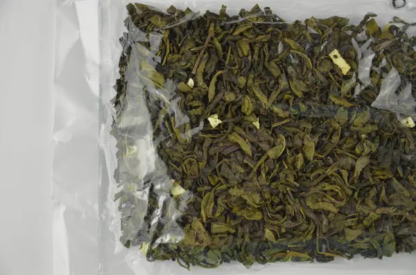 Şeffaf plastik poşette (paket) kuru yeşil yaprak çayı (makro) izole edilmiş üst görünüm