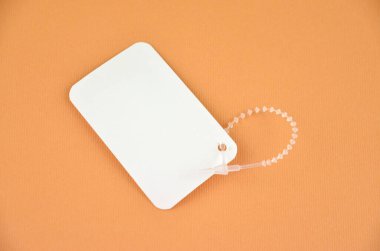 Turuncu zemin üzerinde şeffaf plastik kopçası olan boş beyaz fiyat etiketi, yakın plan