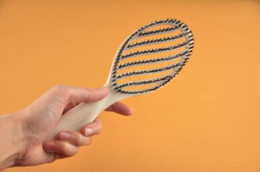 Turuncu arka planda bir elde tüyleri olan yeni bej oval saç fırçası