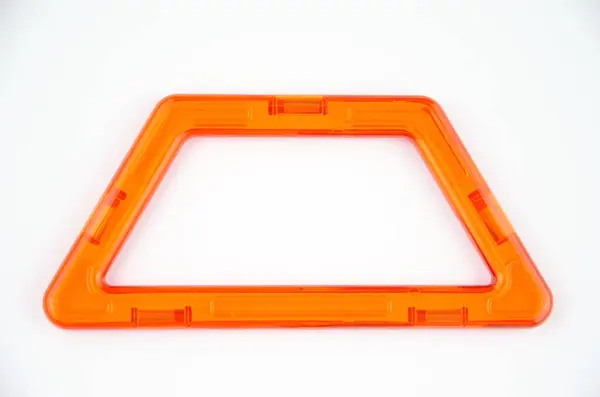 Beyaz arka planda saydam mıknatıs yapıcı kitinden (çocuklar için yapboz oluşturucu) turuncu plastik trapezoid izole edilmiş