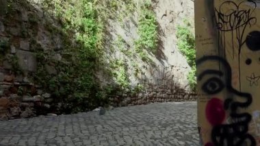 Roma 'da boş bir kaldırım taşlı caddenin orta pozu, canlı sarı binalar ve grafiti sanatıyla, kısmen yemyeşil çimlerle kaplı antik Roma duvarının karşısında, tarihi bir cazibe sergiliyor..