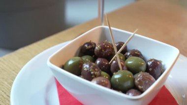 Kırmızı bir peçetenin üzerinde yeşil ve siyah salamura zeytinlerle bembeyaz bir tabağın üzerinde, ahşap bir masanın üzerinde, alkolsüz bir İtalyan içkisi olan Crodino 'nun son derece yakın plan görüntüsü.