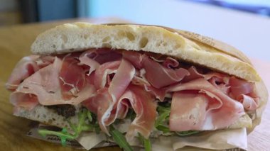 Prosciutto, roket (roka), salsa tartufata (mantar sosu) ve pomodori secchi (güneşte kurutulmuş domates) ile odaklanmış bir sandviçin sağdan sola yakın plan çekimi, İtalyan gurme.