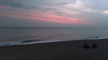 Köpeği olan bir kaç arkadaş, soğuk bir kış öğleden sonrasında Brighton 'ın Güney İngiltere' deki sahil kıyısında oturuyorlar. Güneş batarken berrak gökyüzü parlıyor, ufkun üzerinde kaybolan ışığı yansıtıyor.