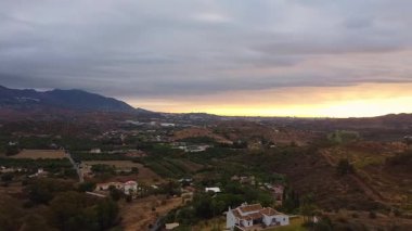 İnsansız hava aracı, sabah erken saatlerde Mijas, Mlaga, İspanya 'da yeşil bir arazide soldan sağa hareket ederek dağları ve canlı pembe-turuncu gündoğumu gökyüzünün altında uzak bir tepeyi gösteriyor..