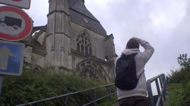 Beauvais, Fransa, 2 Ekim 2024: Bir katedralin arkasındaki basamaklarda duran beyaz adam bulutlu bir öğleden sonra fotoğraf çekiyor, mimarlık ve seyahat anlarını yakalıyor..