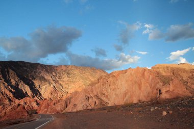 Gün batımında çölün karşısındaki asfalt yol. Kurak vadi boyunca uzanan boş yolun güzel manzarası, kırmızı kum, kumtaşı ve alacakaranlık ışığında kayalık tepeler..