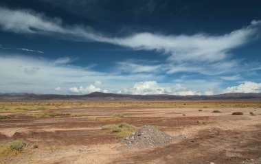 Boşluk. Kurak çöl manzarası, vadi, çimen ve dağ manzarası dramatik bulutlarla dolu güzel mavi bir gökyüzünün altında..