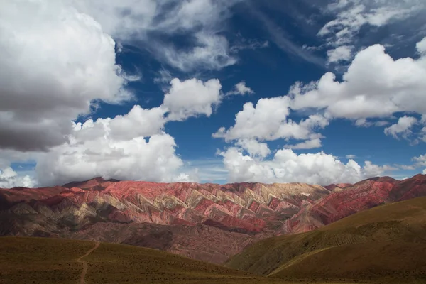 地质学 在阿根廷胡马瓦卡 沿着黄色草原的一条土路 通往五彩斑斓的霍诺卡山 天空阴云密布 引人注目 美丽的岩石和天空质感 — 图库照片