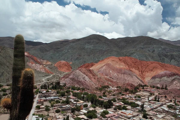 stock image Beautiful view of Purmamarca village at the foot of the popular Seven Color Hill. The buildings and houses, giant cactus Echinopsis atacamensis and Andes mountains under a magical sky.