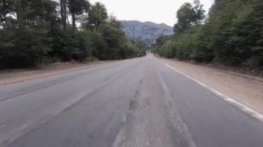 Bulutlu bir günde asfalt otoyol boyunca dağları ve ormanı geçen bir arabanın bakış açısı. 