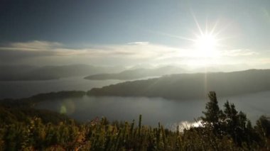 Günbatımında büyülü bir manzaranın panorama görüntüsü. Dağın tepesinden bak. Tepeler, göl, orman ve saklanan güneş bir mercek patlaması yaratıyor. Güzel Patagonya sonbahar renkleri.