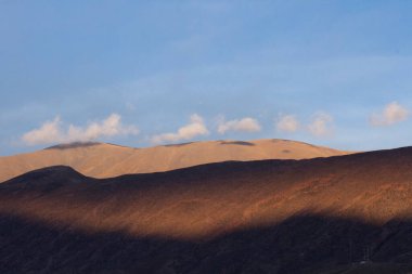 Şiirsel doğal arka plan. Gün batımında mavi gökyüzünün altındaki And Dağları 'nın manzarası. Dağlardaki güzel güneş ışığı ve gölge kontrastı. 