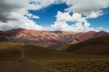 Sarı çayırlar boyunca yürüyüş. Renkli Hornocal dağına uzanan, bulutlu gökyüzünün altındaki, altın vadiden geçen bir patikanın manzarası..