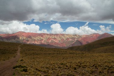 Yürüyüş. Altın vadiyi boydan boya geçen renkli Hornocal dağına doğru dramatik bir bulutun altında giden bir yol. Güzel kaya dokusu.