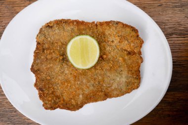 Arjantin yemeği. Milanesa manzarası, kızarmış biftek, bir dilim limon ve patates püresi, ahşap arka planda beyaz bir tabakta.. 