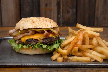 Lezzetli hamburger. Çedar peyniri, salatalık ve kızarmış domuz pastırmalı hamburger, patates kızartması ve ahşap bir arka plan.. 