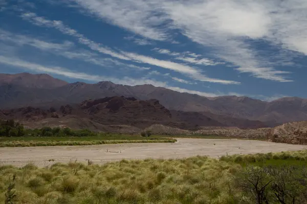 Stock image Rural landscape. View of the green meadow, grasses, sand desert and mountains in the background under a beautiful blue sky with clouds. 