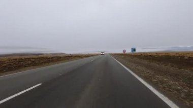 Sabahın erken saatlerinde, asfalt kırsal yol boyunca sarı çayır ve tepelerden geçen bir arabanın bakış açısı. 