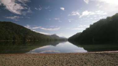 Güneşli bir günde kumlu göl, orman ve dağların manzarası. Su yüzeyinde güzel bir çevre yansıması.
