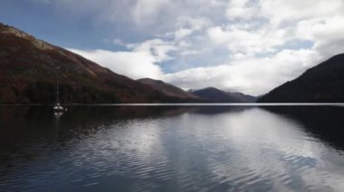 Seyahat et. Sakin göldeki bir yelkenli teknesinin büyüleyici manzarası. Sonbaharda orman ve ufukta dağlar. Güzel gökyüzü ve tepeler su yüzeyinde yansıyor..
