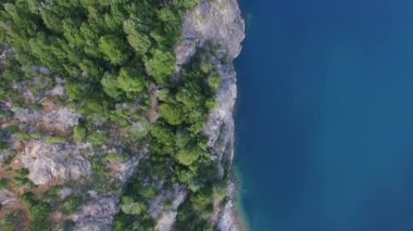 Büyülü manzara. Dik kayalıkların, ormanın ve gölün yukarıdan görünüşü. Su yüzeyinde güzel mavi gökyüzü yansıması.