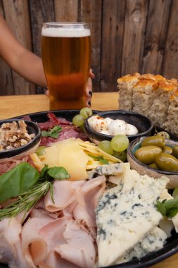 Restoran masasında yemek var. Ahşap arka planda farklı tabakların yakın görüntüsü. Dilimlenmiş salam, peynir, mavi peynir, Focaccia ekmeği, İtalyan boconccinosu, ceviz, jambon, pişirilmiş jambon ve ahşap masada yeşil zeytin..              