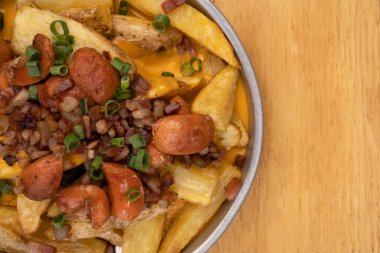 Dilimlenmiş yeşil soğanlı kızarmış patates, füme sosis, çıtır pastırma ve çedar peyniri sosu, ahşap masadaki metal bir tabakta yakın plan görüntüsü..