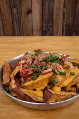 Dilimlenmiş yeşil soğanlı kızarmış patates, füme sosis, çıtır pastırma ve çedar peyniri sosu, ahşap masadaki metal bir tabakta yakın plan görüntüsü..