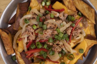 Dilimlenmiş yeşil soğanlı kızarmış patates, füme sosis, çıtır pastırma ve çedar peyniri sosu, ahşap masadaki metal bir tabakta yakın plan görüntüsü..