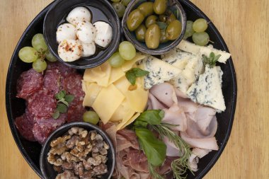 Restoran masasında yemek var. Ahşap arka planda farklı tabakların yakın görüntüsü. Dilimlenmiş salam, peynir, mavi peynir, Focaccia ekmeği, İtalyan boconccinosu, ceviz, jambon, pişirilmiş jambon ve ahşap masada yeşil zeytin..              