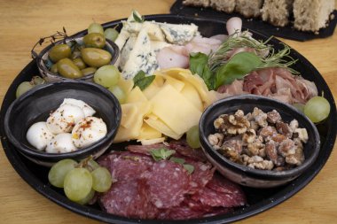 Restoran masasında yemek var. Ahşap arka planda farklı tabakların yakın görüntüsü. Dilimlenmiş salam, peynir, mavi peynir, Focaccia ekmeği, İtalyan boconccinosu, ceviz, jambon, pişirilmiş jambon ve ahşap masada yeşil zeytin..              