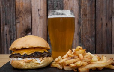 Geleneksel çizburger, çedar, soğan, patates kızartması ve bir bardak bira..