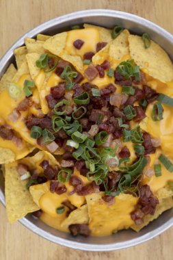 Çedar arkaplanlı cips. Çedar peynirli nachos, yeşil soğan ve ahşap bir tabakta gevrek domuz pastırması..