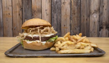 Bitki bazlı burger. Burger değil. NotCo hamburgerin yakın plan görüntüsü, marul, çıtır soğan halkaları, peynir, Notco mayonez ve patates kızartması, ahşap arka planda metal bir çanak içinde..