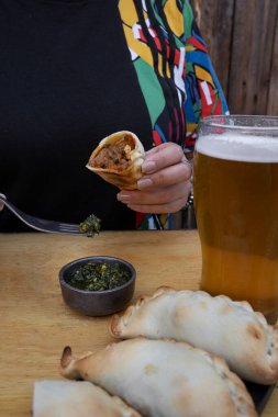 Restoranda börek yiyorum. Geleneksel chimichurri soslu et böreği yiyen ve bir bardak bira içen bir kadın..